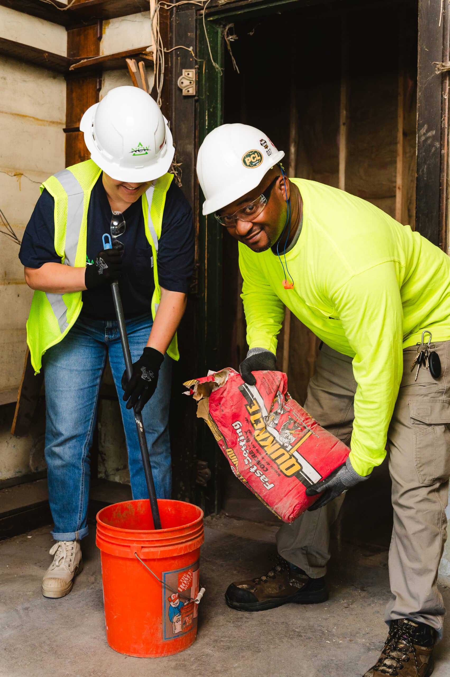 Two construction workers in personal protective equipment prepare concrete to be poured at their job site.