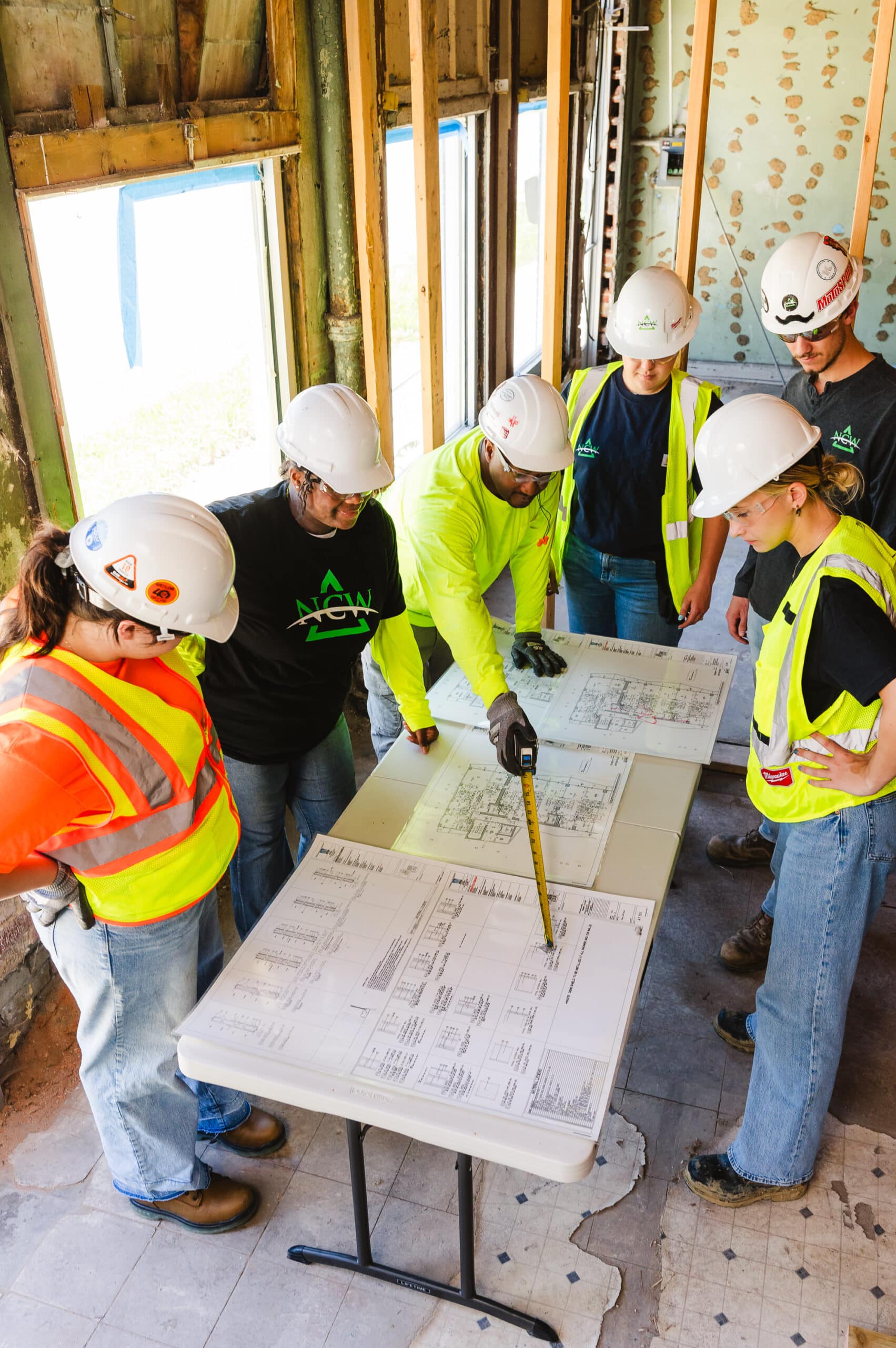 A group of construction workers are shown their day's tasks by their superintendent.