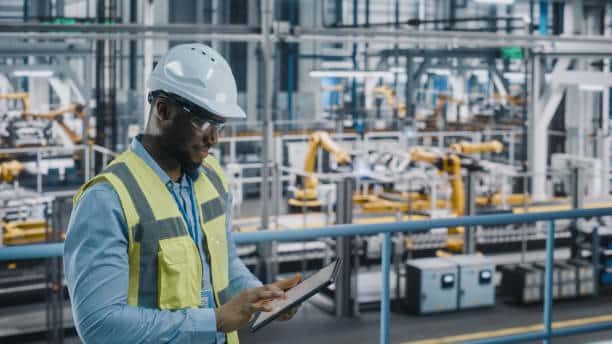 Happy Car Factory Engineer in High Visibility Vest Using Tablet Computer. Automotive Industrial Facility Working on Vehicle Production on Automated Technology Assembly Plant.